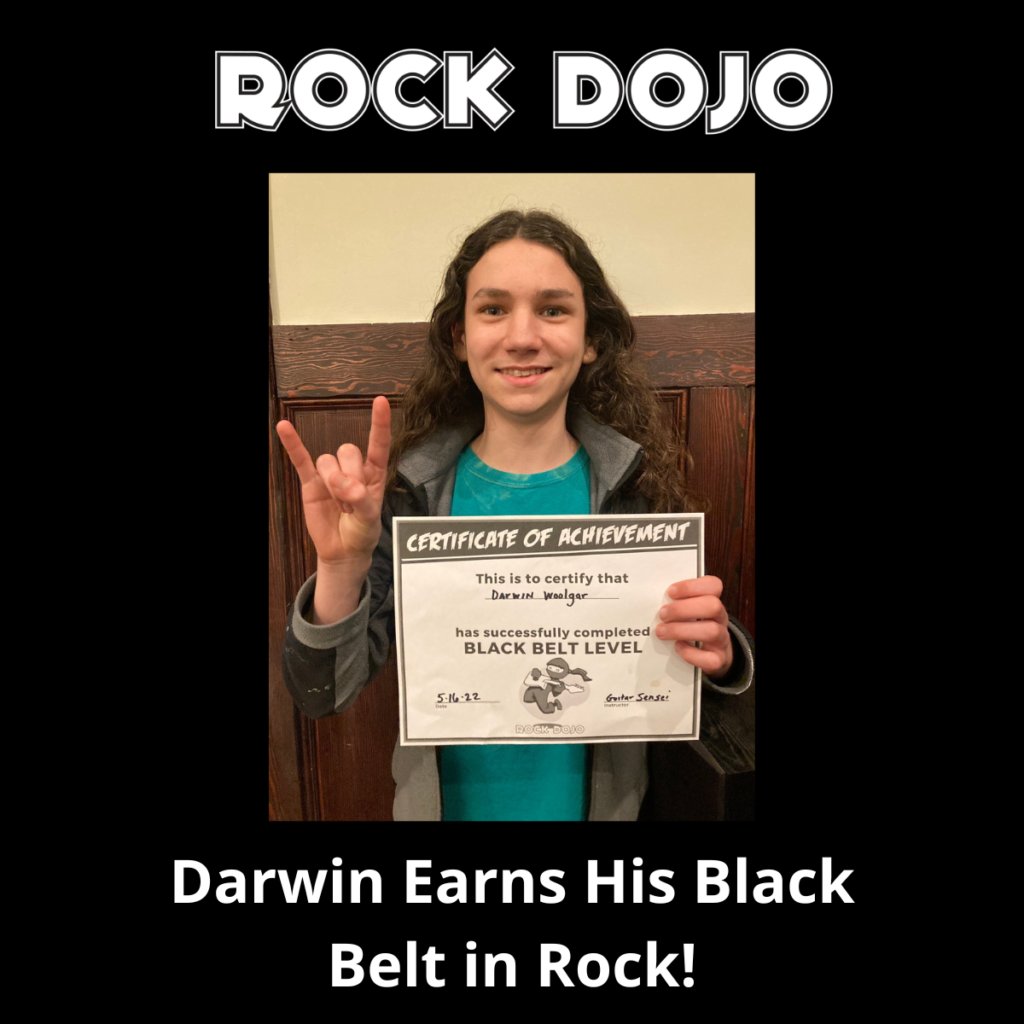 Darwin holding up his certificate of completion representing his black belt in rock guitar through the Rock Dojo online course.
